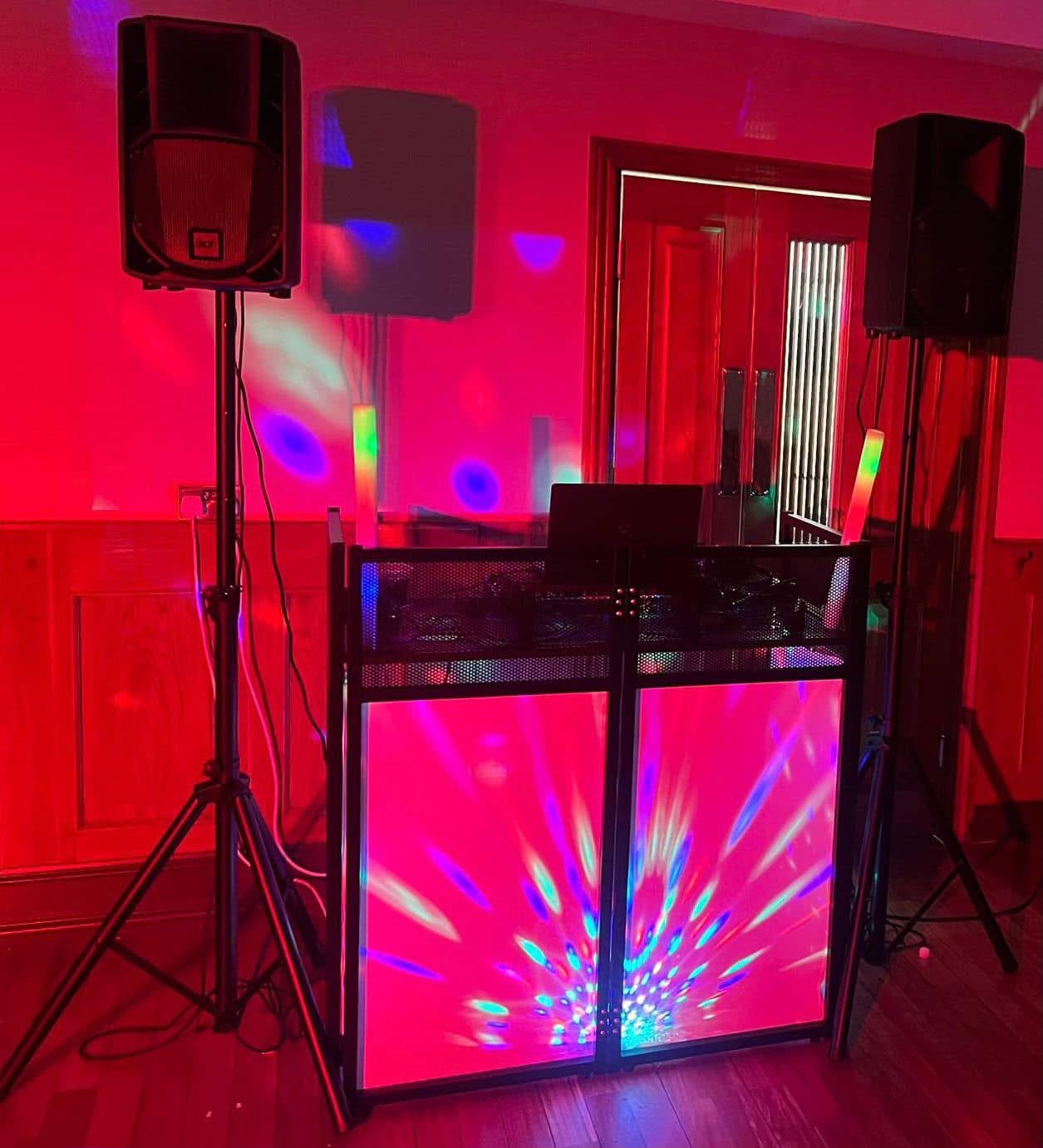 DJ setup with a light-up facade and disco lighting under red uplighting