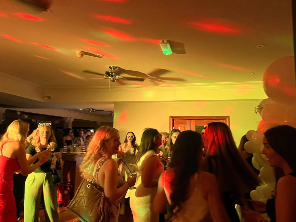 Packed dance floor of guests dancing under green party lighting
