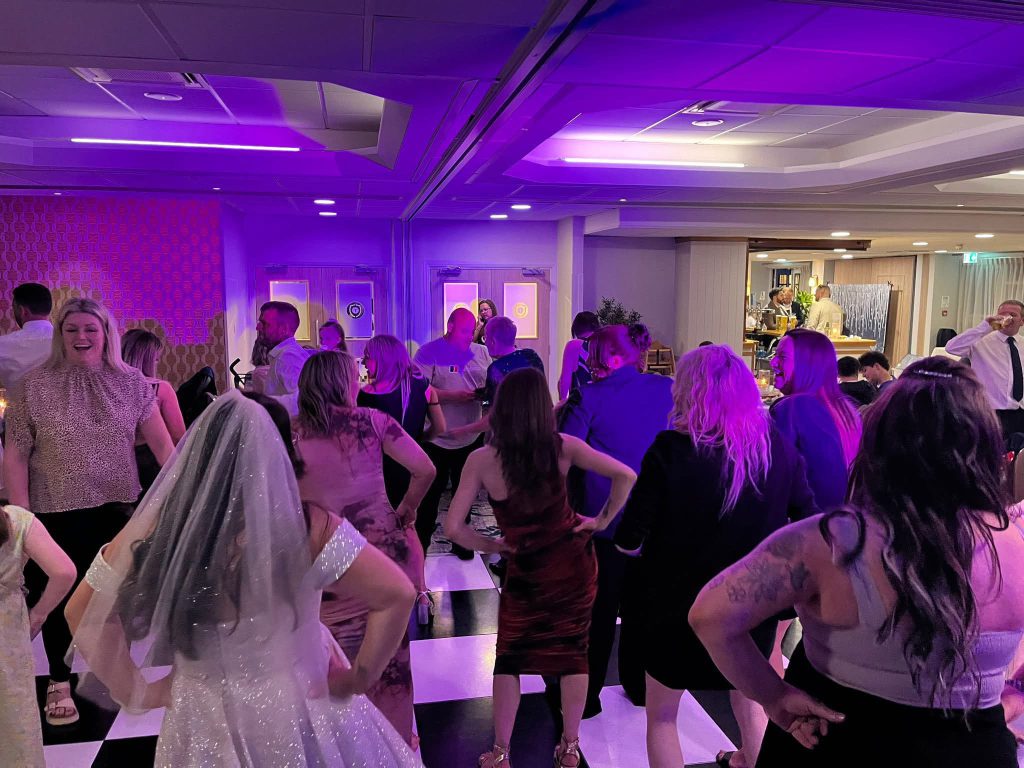 Wedding guests dancing under purple lighting on a chequered dance floor